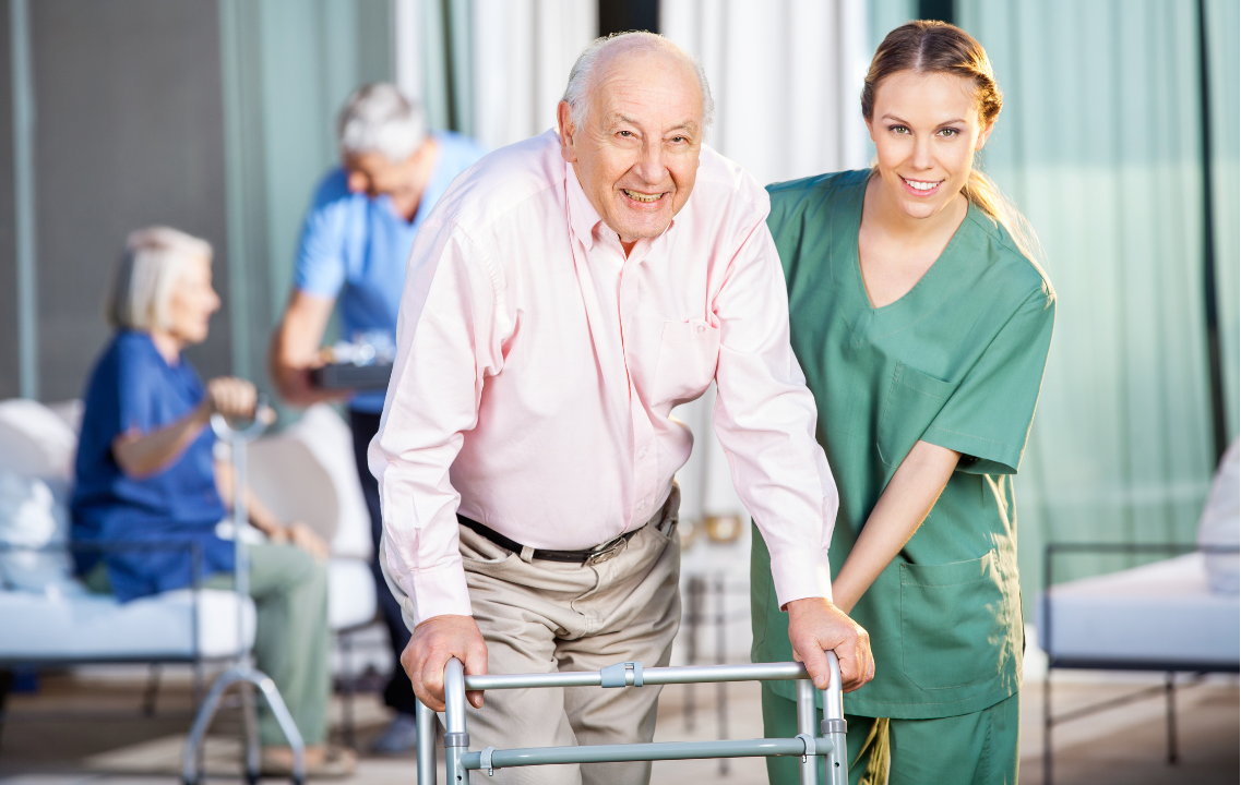 Certified nursing assistant helping an older adult walk safely with a walker in a long-term care setting.